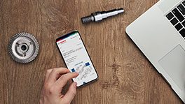 木製のテーブルの上にスマートフォンがあり、その隣にノートパソコンのキーボードと工具があります。