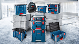 灰色の背景に赤いアクセントがある青い工具箱の配置、コンクリートブロックに囲まれています。背景にはリュックサックが見えます。