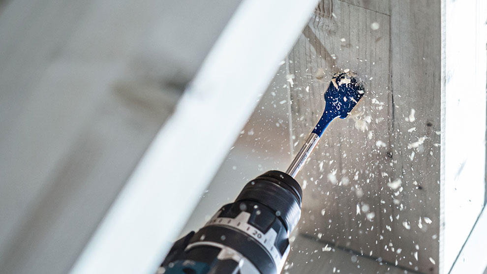 木材用 青いボッシュプロフェッショナルドリルが木材を貫通し、木くずが飛び散る。