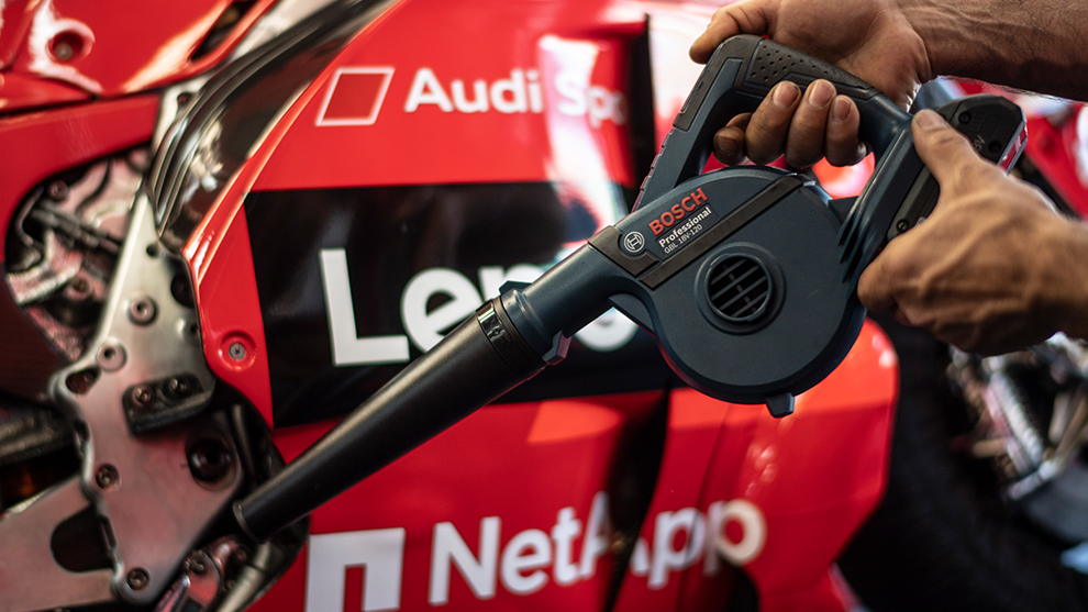 ある人が赤いレーシングカーの前でボッシュプロフェッショナルのヘアドライヤーを持っています。