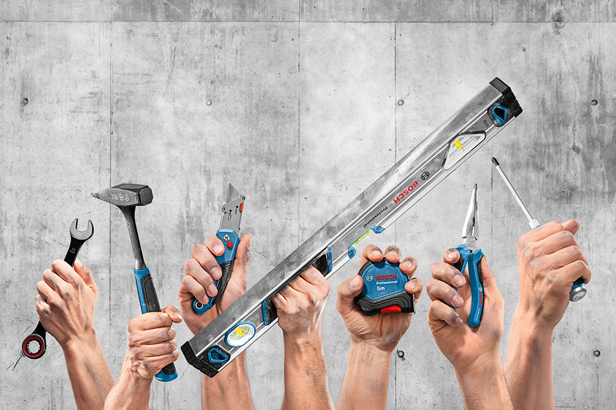 手がコンクリートの壁の前でさまざまなボッシュプロフェッショナルツールを持っています。