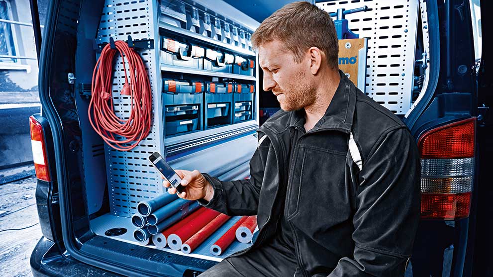 黒い服を着た職人がバンに座って携帯電話を見ています。