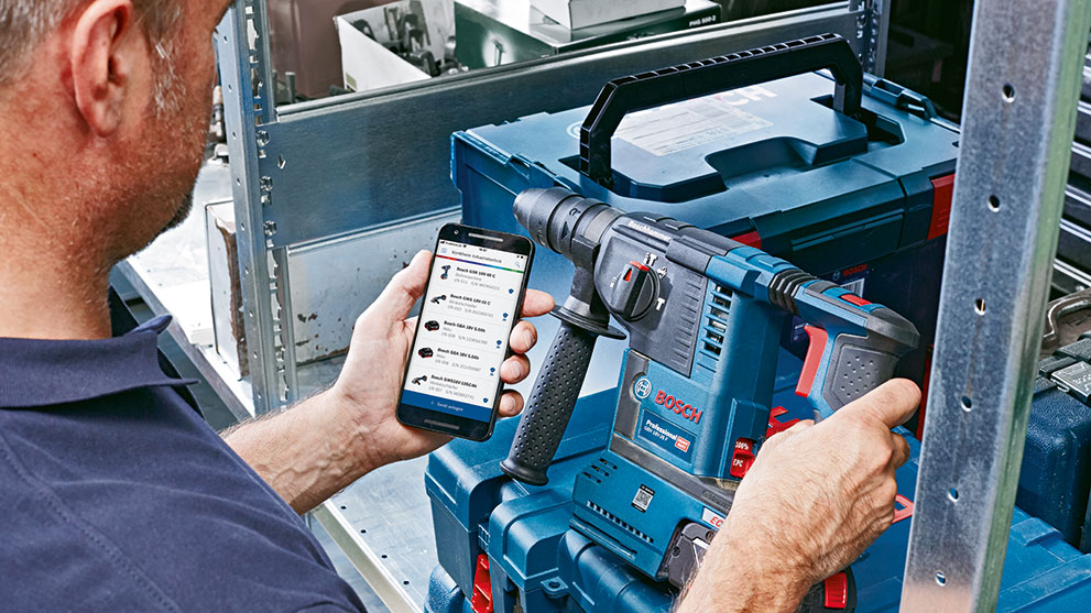 男性が青いボッシュプロフェッショナルドリルを持ち、スマートフォンを見ています。