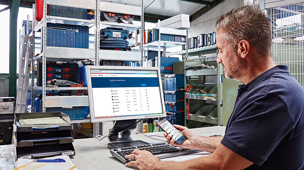 男性が作業場でコンピュータとスマートフォンを使用しています。