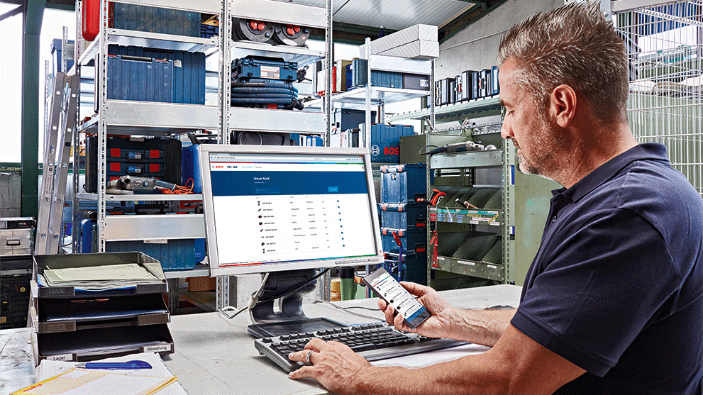 コンピュータの前にいる男性、背景にボッシュの工具があり、スマートフォンを使用しています。