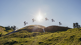 自転車に乗った人が日光の下で丘を飛び越え、緑の草に囲まれています。