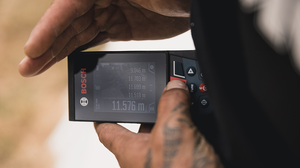 手がディスプレイ付きのボッシュプロフェッショナルレーザー距離計を持っています。