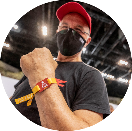 マスクをした男性がカラフルなブレスレットを見せて微笑んでいます。