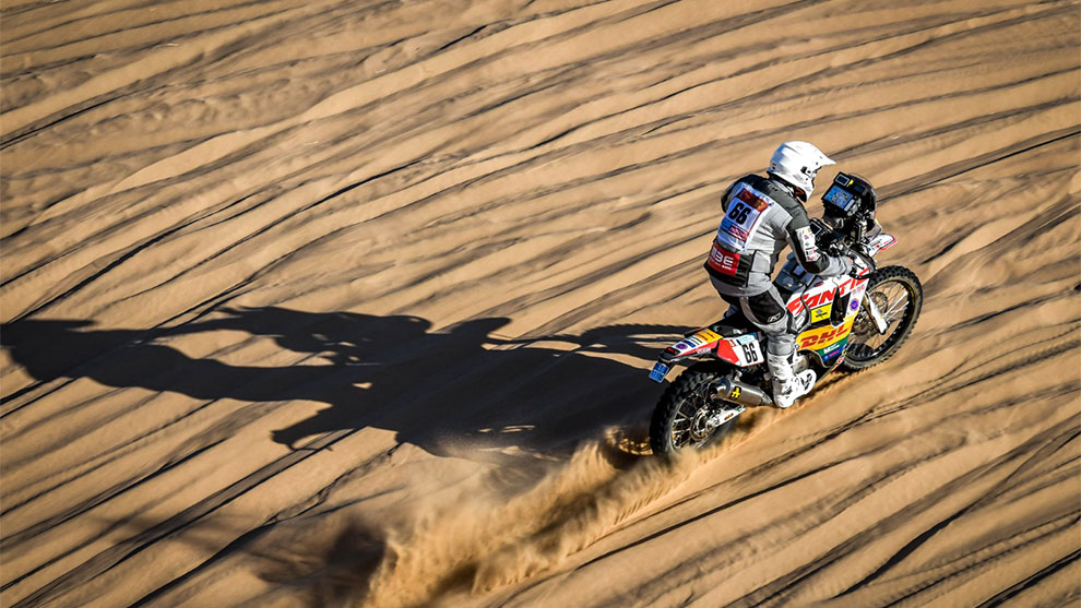 砂の上のバイクライダー、跡を残し、太陽が長い影を落とす。