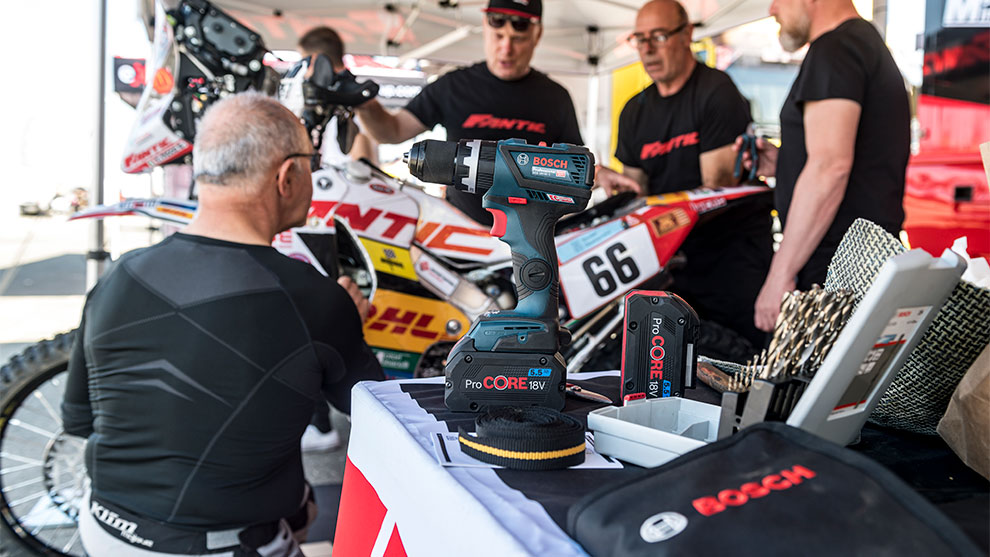 ボッシュプロフェッショナルのコードレスドライバーがテーブルの上にあり、前景にはメカニックがいます。