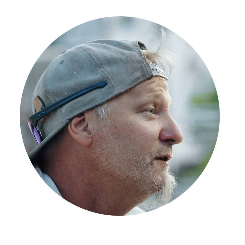 灰色のキャップをかぶった男性が話していて、顔は横を向いて微笑んでいます。