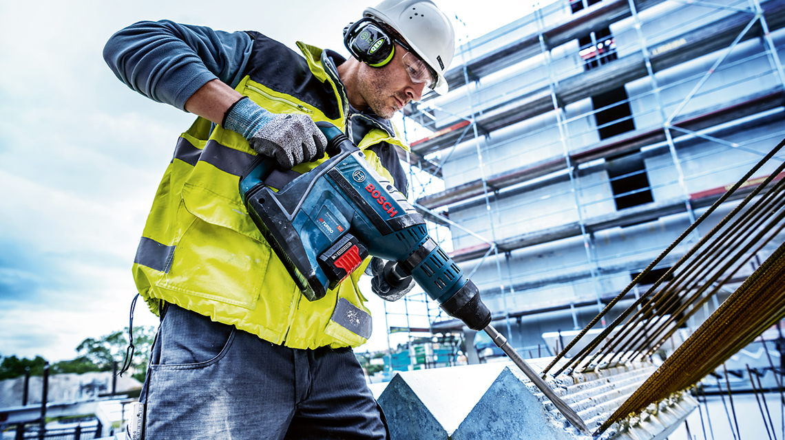 黄色の警告ジャケットを着た作業者がボッシュの工具で穴を開けています。