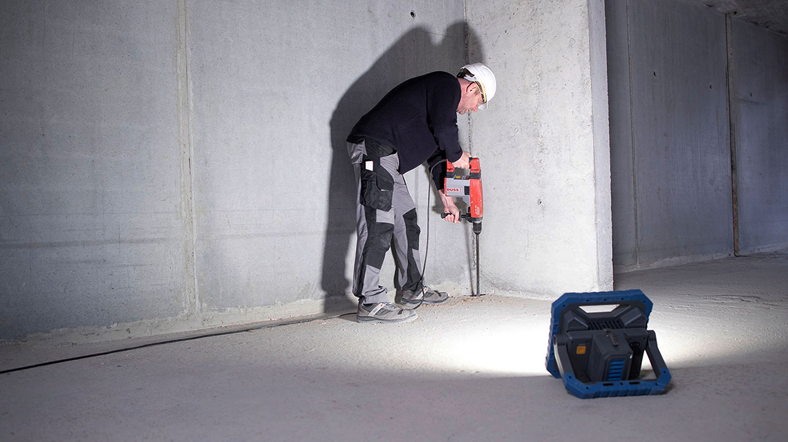 赤いボッシュプロフェッショナルドリルを持った作業者が壁を加工しています。
