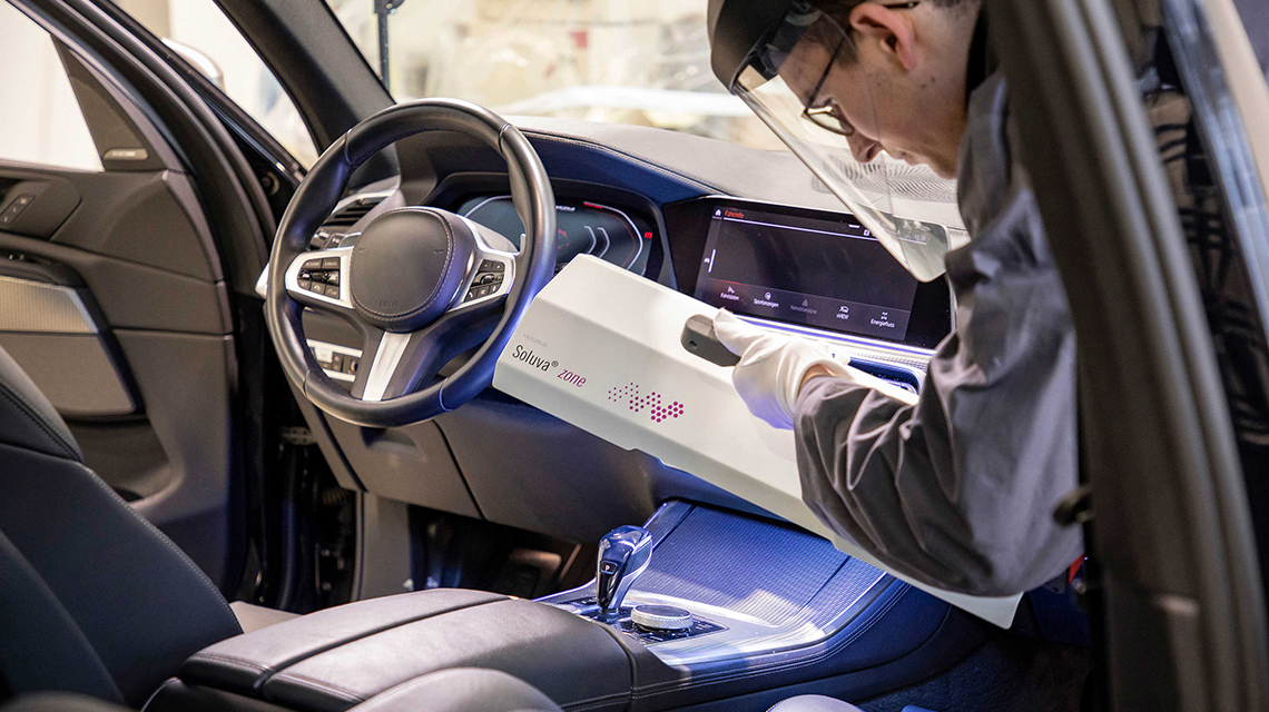 防護服を着た男性が車のダッシュボードを消毒しています。