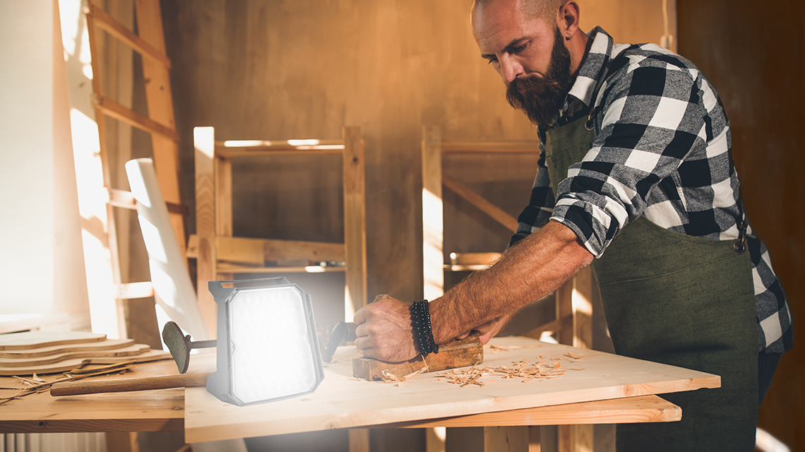 男性がテーブルで木材を加工しており、明るいランプが光を放っています。
