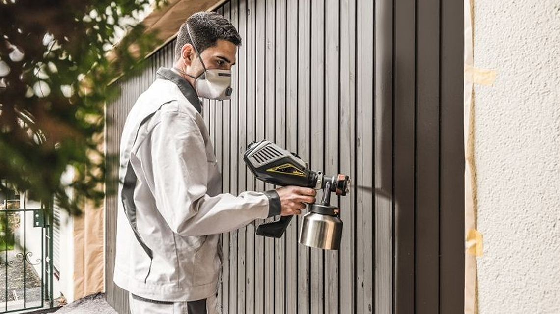 作業服を着た男性が壁に木材用ペイントをスプレーしています。