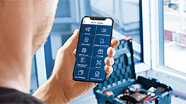 男性がアプリを使ったスマートフォンを手に持ち、背景にはスーツケースがあります。